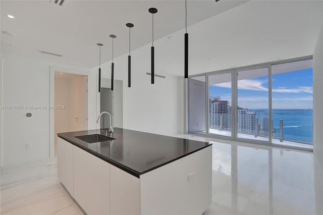 kitchen with hanging light fixtures, sink, white cabinetry, floor to ceiling windows, and a water view