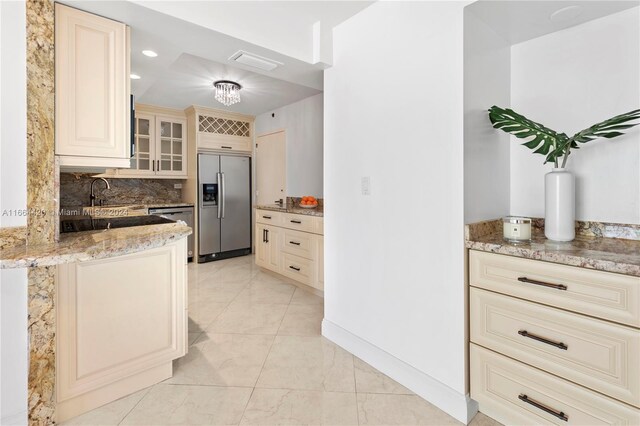 kitchen featuring sink, tasteful backsplash, cream cabinetry, stainless steel appliances, and light stone countertops