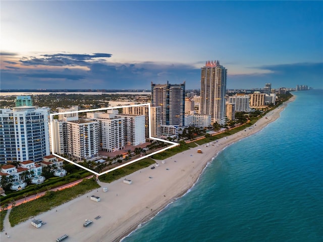 aerial view at dusk featuring a view of the beach and a water view