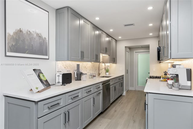 kitchen with gray cabinetry, sink, light hardwood / wood-style flooring, and stainless steel dishwasher