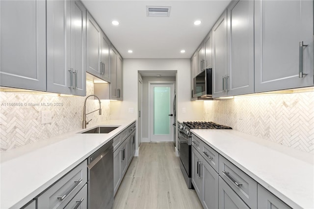 kitchen with sink, light hardwood / wood-style flooring, gray cabinets, stainless steel appliances, and tasteful backsplash