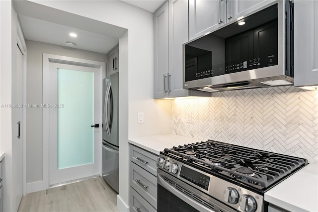 kitchen featuring light stone counters, backsplash, stainless steel appliances, and light wood-type flooring