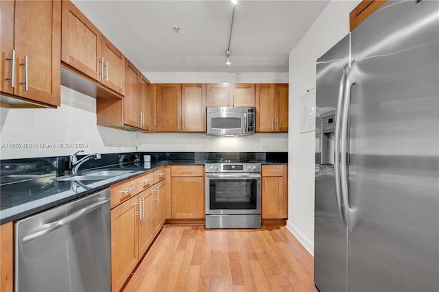 kitchen with dark stone counters, light hardwood / wood-style floors, appliances with stainless steel finishes, and sink