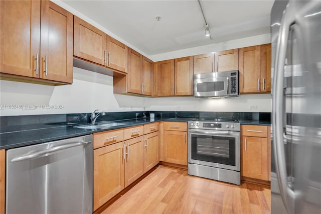 kitchen with light hardwood / wood-style floors, track lighting, sink, appliances with stainless steel finishes, and dark stone countertops