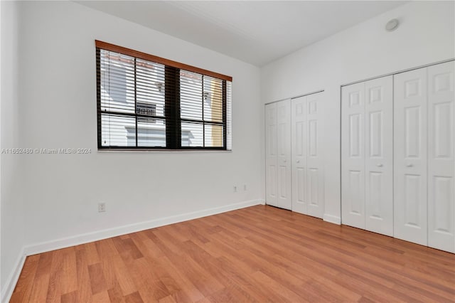 unfurnished bedroom with light hardwood / wood-style floors and two closets