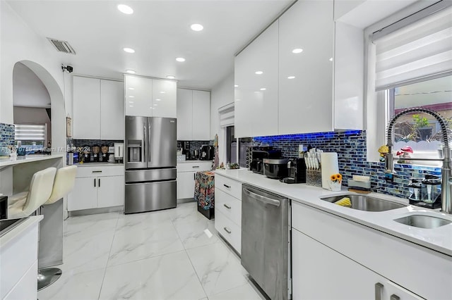 kitchen with appliances with stainless steel finishes, sink, tasteful backsplash, and white cabinetry