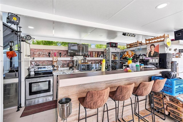 kitchen with kitchen peninsula, electric stove, light tile patterned floors, and plenty of natural light