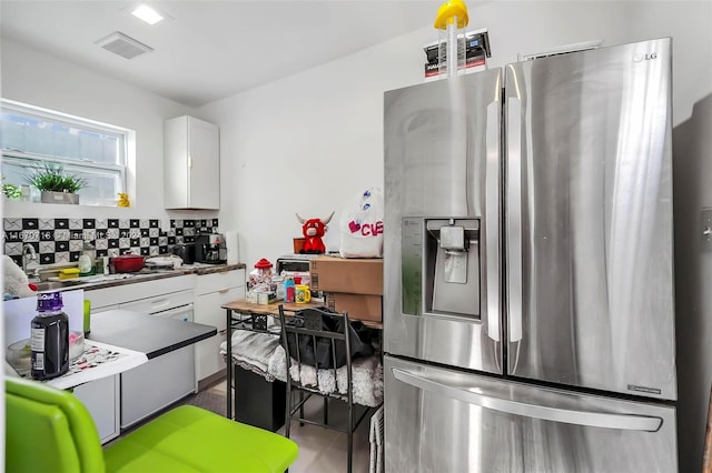 kitchen featuring white cabinets, stainless steel refrigerator with ice dispenser, and tasteful backsplash