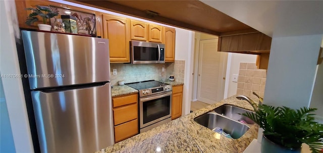 kitchen featuring light stone countertops, stainless steel appliances, backsplash, and sink