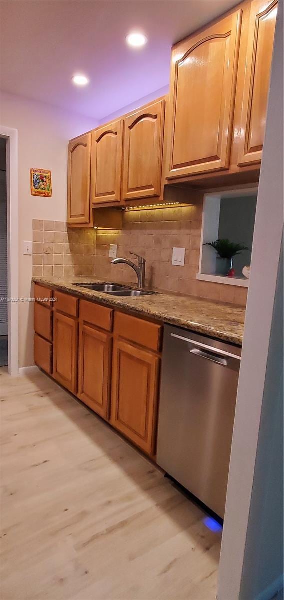 kitchen with light stone countertops, dishwasher, decorative backsplash, sink, and light wood-type flooring