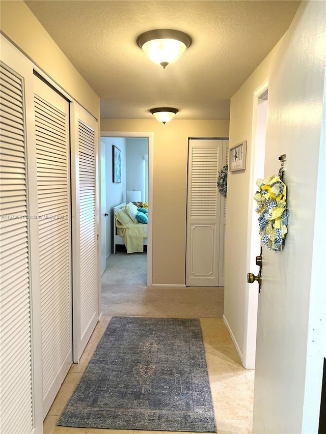 corridor featuring a textured ceiling and light carpet