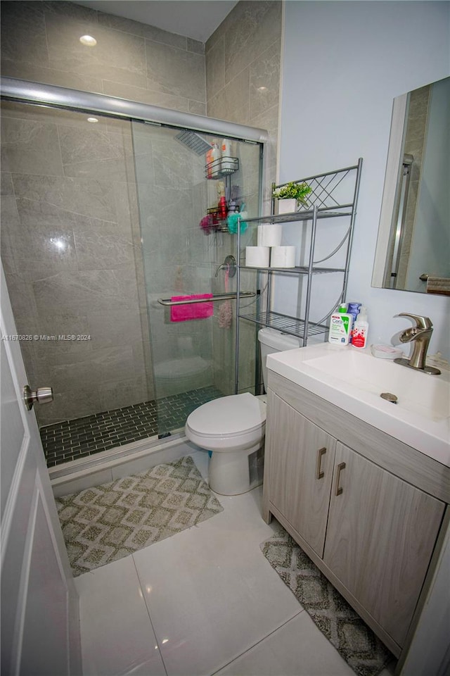 bathroom featuring tile patterned flooring, a shower with door, vanity, and toilet