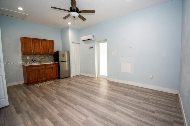 kitchen with light wood-type flooring, tasteful backsplash, a wall mounted AC, ceiling fan, and stainless steel fridge