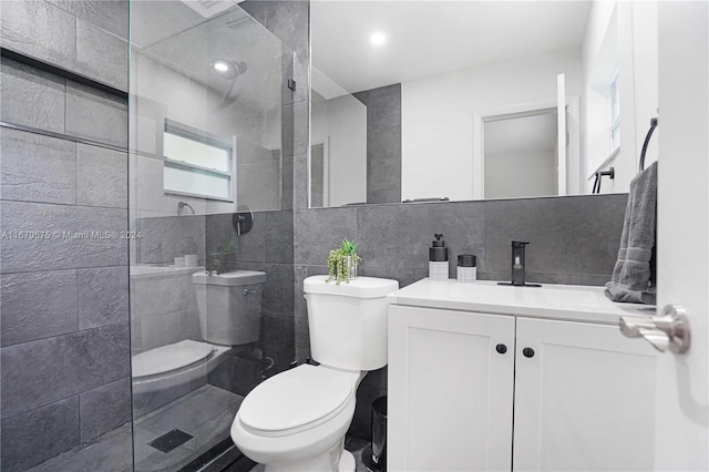 bathroom with a tile shower, vanity, toilet, and tile walls