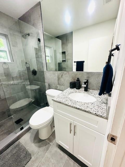 bathroom featuring tiled shower, vanity, tile walls, and toilet