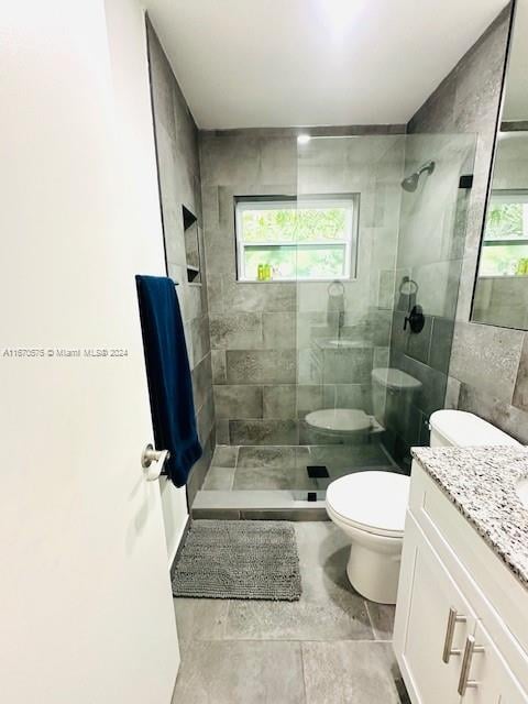 bathroom with a tile shower, vanity, and toilet