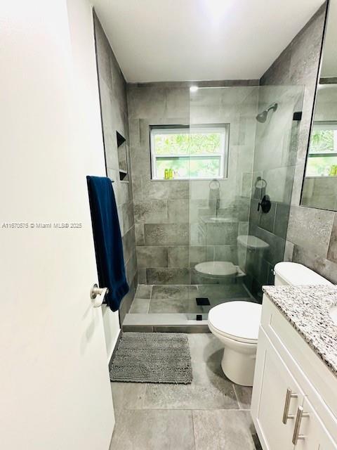 bathroom featuring a tile shower, toilet, and vanity