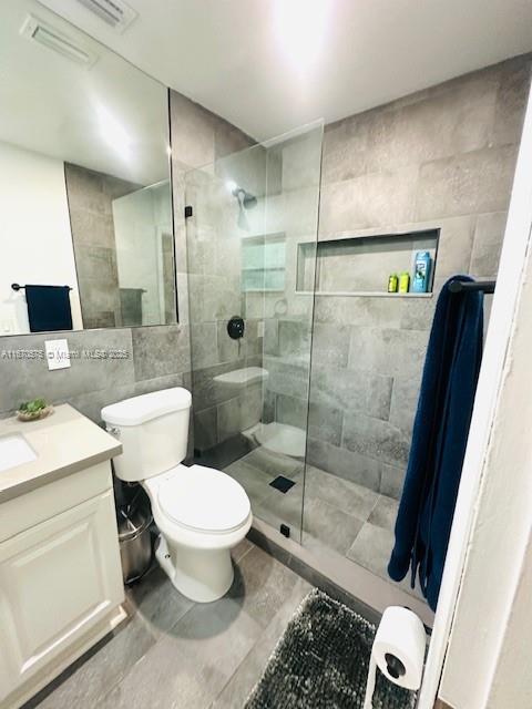 bathroom featuring tile walls, tiled shower, vanity, and toilet