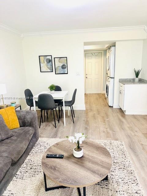 living room featuring stacked washer / drying machine, crown molding, and light wood-type flooring