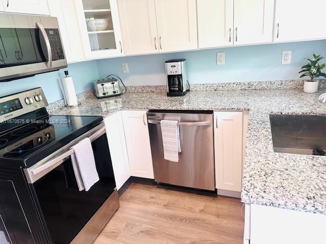 kitchen with appliances with stainless steel finishes, light stone counters, sink, white cabinets, and light hardwood / wood-style floors