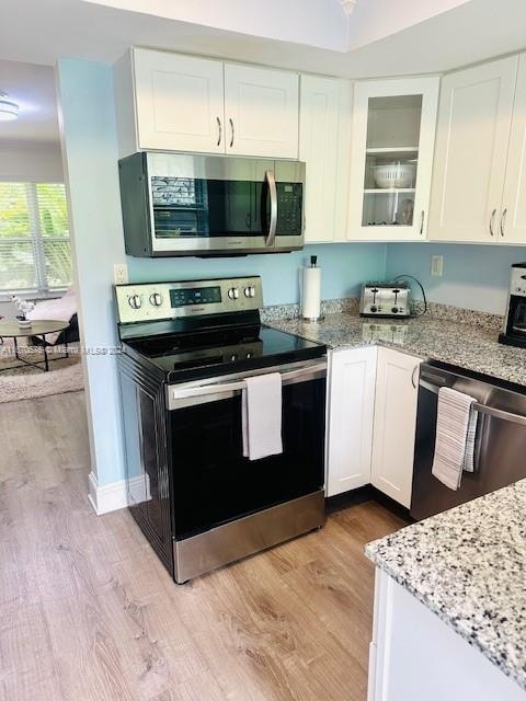 kitchen with white cabinets, light hardwood / wood-style floors, light stone counters, and appliances with stainless steel finishes