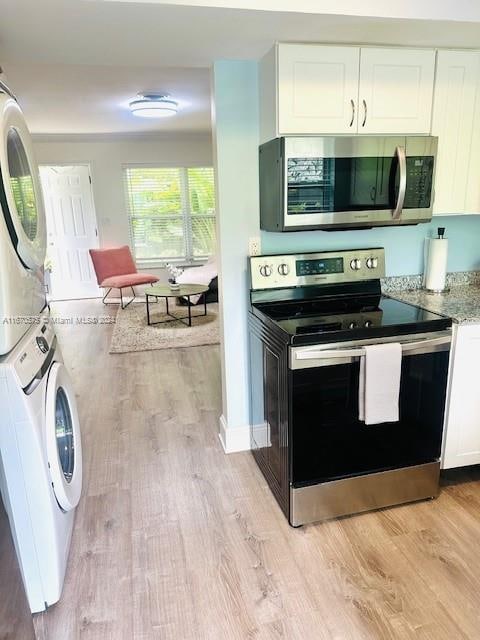 kitchen featuring white cabinetry, light wood-type flooring, stacked washer and dryer, and stainless steel appliances