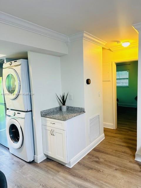 clothes washing area featuring light wood-type flooring, stacked washer and clothes dryer, and ornamental molding