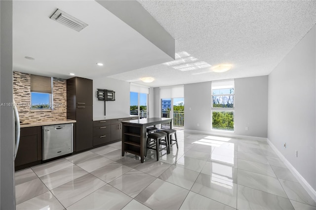 kitchen with tasteful backsplash, a kitchen island, a textured ceiling, dark brown cabinetry, and stainless steel dishwasher