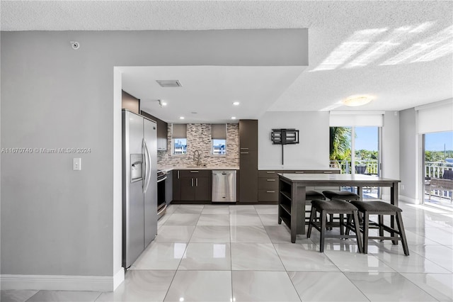 kitchen with a textured ceiling, appliances with stainless steel finishes, tasteful backsplash, and light tile patterned flooring