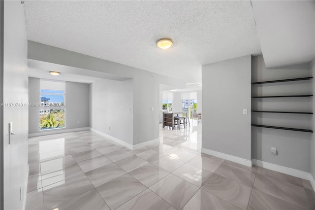 empty room with a wealth of natural light, a textured ceiling, and light tile patterned flooring