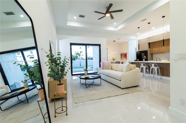 living room featuring ceiling fan, light tile patterned flooring, and a tray ceiling