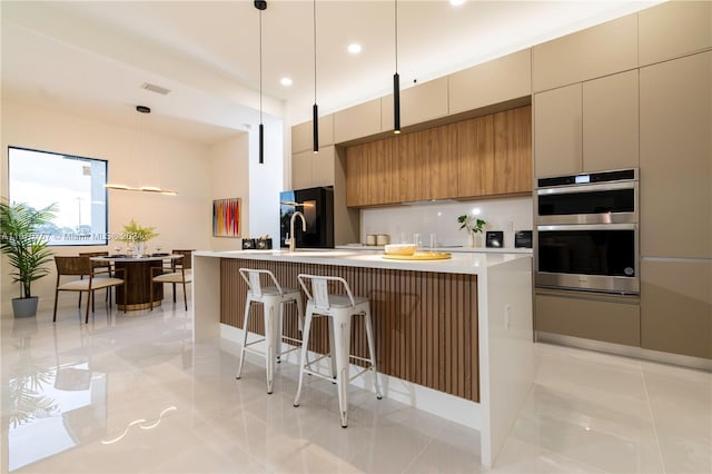 kitchen featuring black fridge, an island with sink, hanging light fixtures, double oven, and a breakfast bar