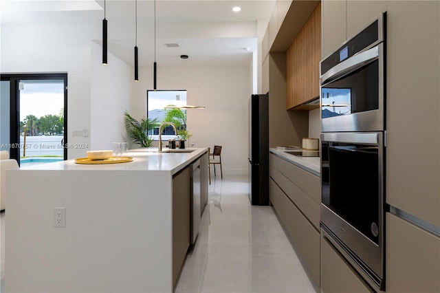 kitchen with pendant lighting, sink, a kitchen island with sink, double oven, and black refrigerator