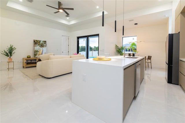 kitchen with a kitchen island with sink, pendant lighting, a raised ceiling, sink, and stainless steel appliances