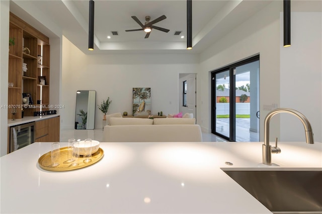 kitchen featuring a raised ceiling, wine cooler, sink, and ceiling fan