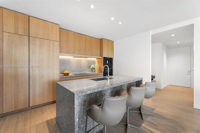 kitchen with a center island with sink, light hardwood / wood-style floors, sink, and light stone countertops