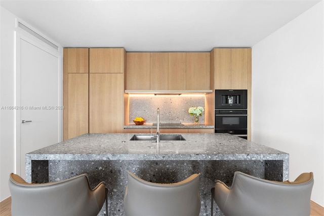 kitchen with light stone counters, black oven, light hardwood / wood-style flooring, and sink