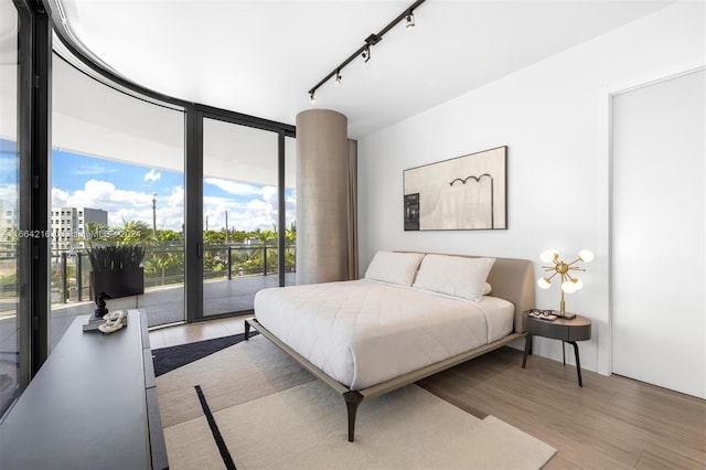 bedroom with light wood-type flooring, track lighting, access to exterior, and floor to ceiling windows