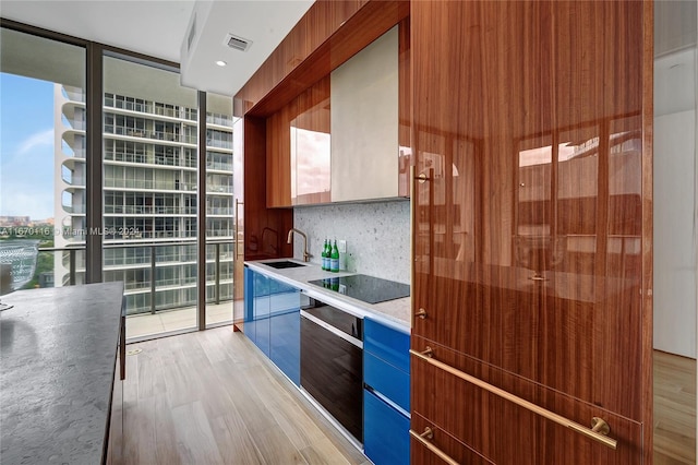 kitchen with sink, light hardwood / wood-style flooring, expansive windows, backsplash, and black electric cooktop