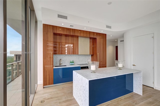 kitchen featuring tasteful backsplash, light hardwood / wood-style flooring, a kitchen island, and sink