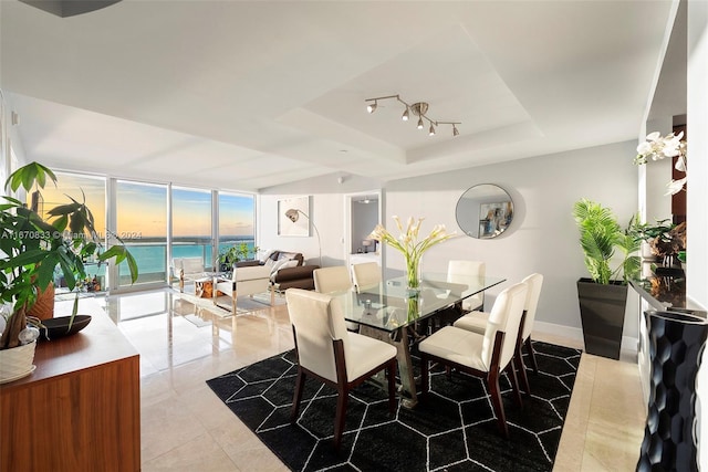 dining area featuring a water view, a tray ceiling, expansive windows, and light tile patterned flooring