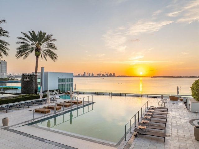 pool at dusk with a patio and a water view