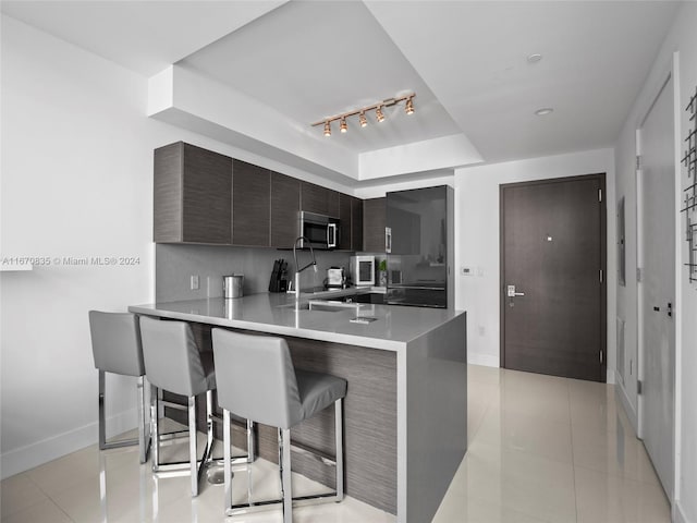 kitchen with decorative backsplash, kitchen peninsula, light tile patterned flooring, and a kitchen breakfast bar