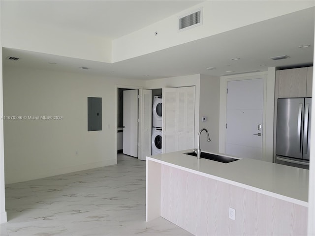 kitchen with electric panel, stainless steel refrigerator, stacked washer / drying machine, light brown cabinetry, and sink