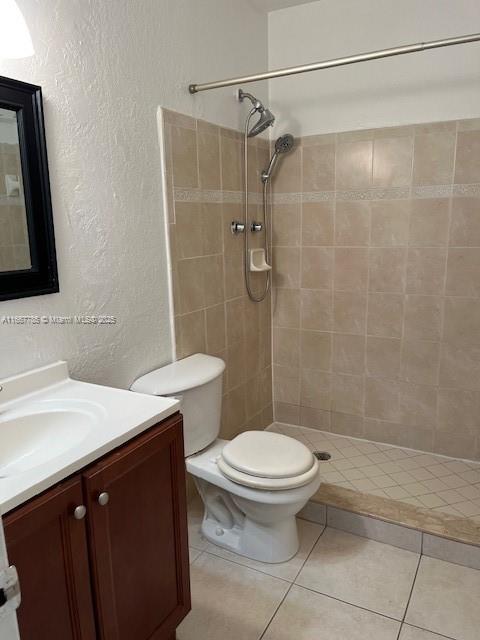 bathroom with vanity, tile patterned flooring, toilet, and a tile shower