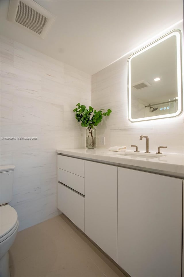 bathroom featuring toilet, tile patterned flooring, vanity, and tile walls