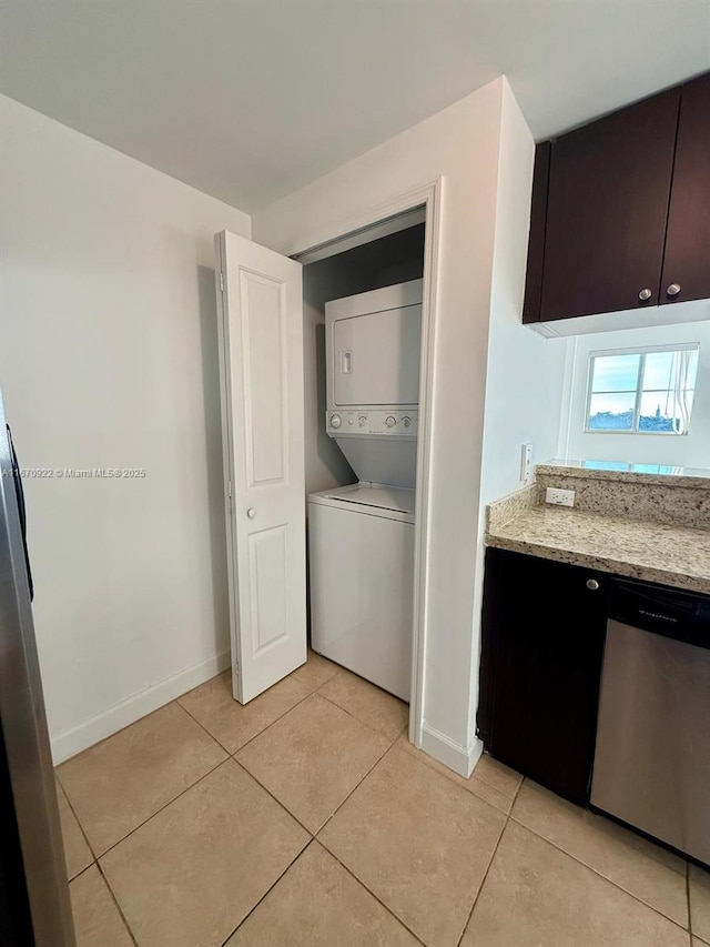 washroom featuring stacked washer / drying machine, laundry area, baseboards, and light tile patterned floors