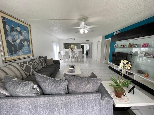 living room with ceiling fan, a textured ceiling, and light tile patterned flooring