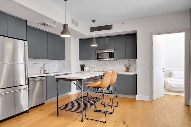 kitchen featuring backsplash, appliances with stainless steel finishes, hanging light fixtures, sink, and light hardwood / wood-style flooring