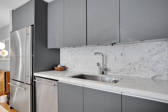 kitchen featuring stainless steel appliances, light stone counters, decorative backsplash, sink, and gray cabinetry